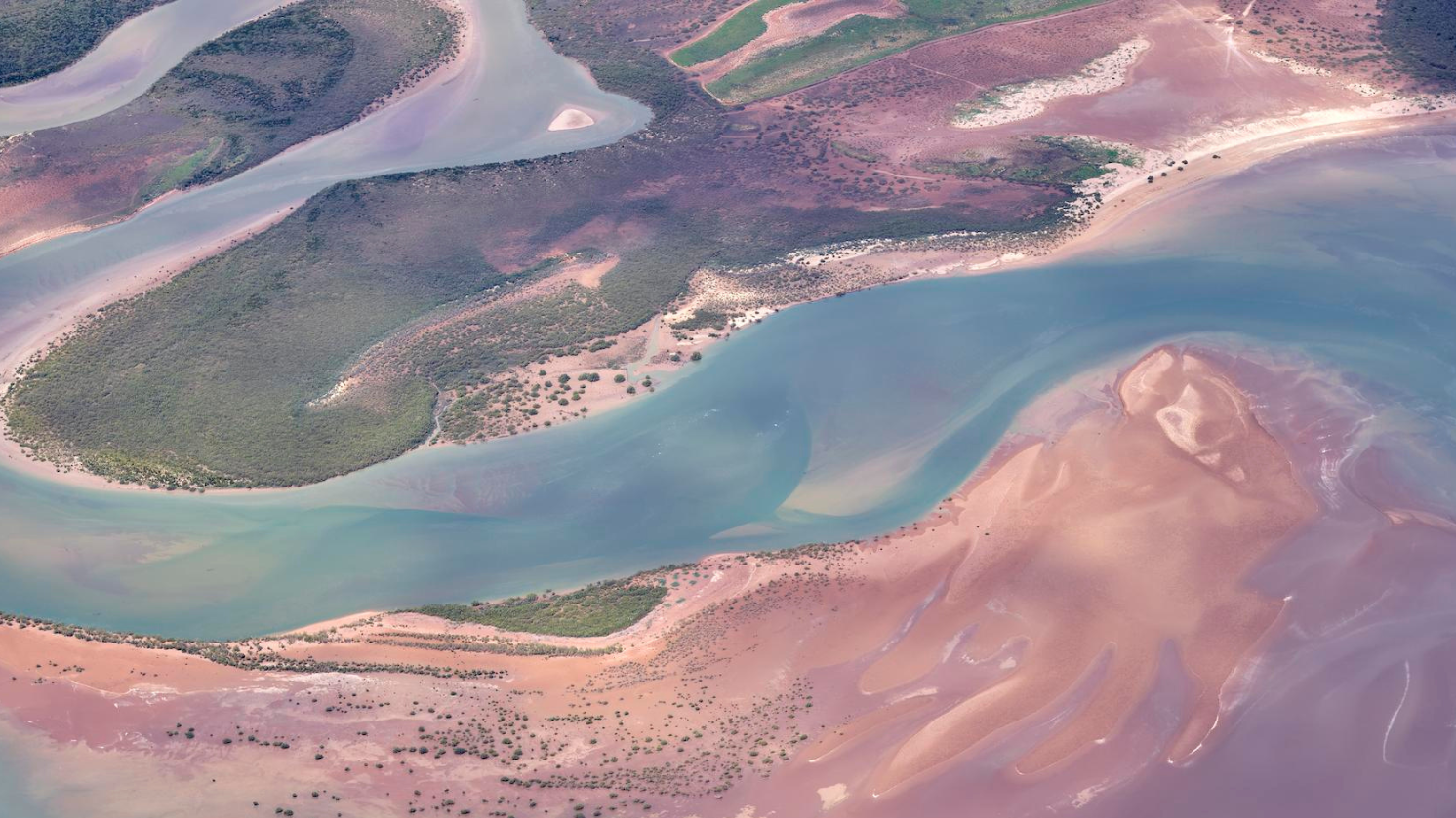 A beautiful aerial image of a Port Hedland land and seascape in Western Australia – showing the captivating pink, green and blue hues created as the inlet meets the Indian Ocean.